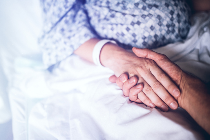 A woman in labor prepares to give birth in a clean white hospital setting, holding the hand of her husband or partner. Detail shot of their hands being held on the white hospital bed linens. A depiction of love and support during pregnancy or any hospital stay. Horizontal image with copy space.