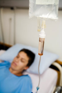 Patient in bed with drip bag, regulator and tubing.