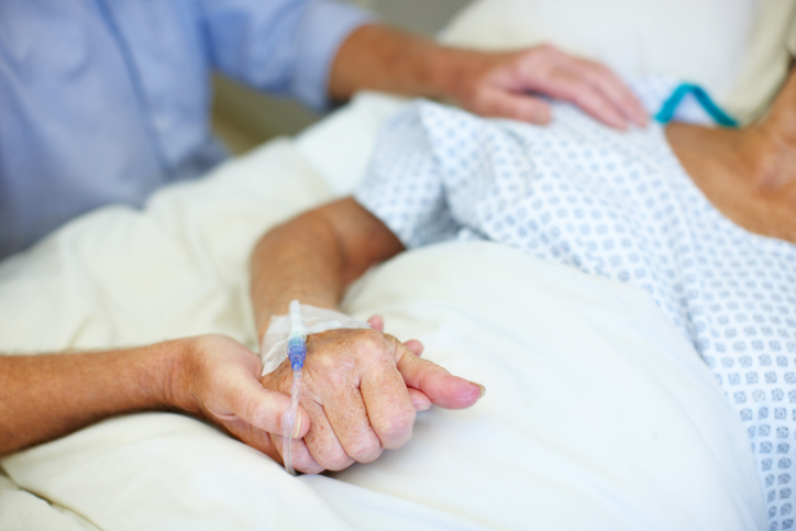 Closeup shot of an elderly man holding his wife's hand while she is ill in the hospital