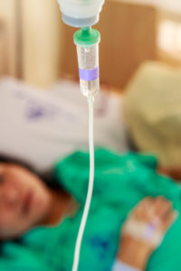 Close up of IV bag with patient in bed in the background.