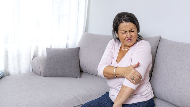 Old woman hand holding her elbow suffering from elbow pain. File contains a clipping path. Senior woman suffering from pain in hand at home. Old age, health problem and people concept